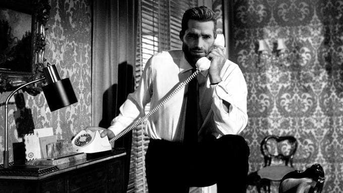 Man in a suit talking on a telephone in black and white.