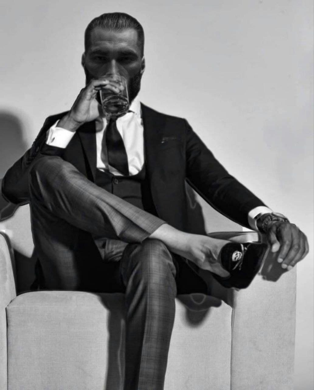 Confident man in a suit sipping a drink in an armchair.