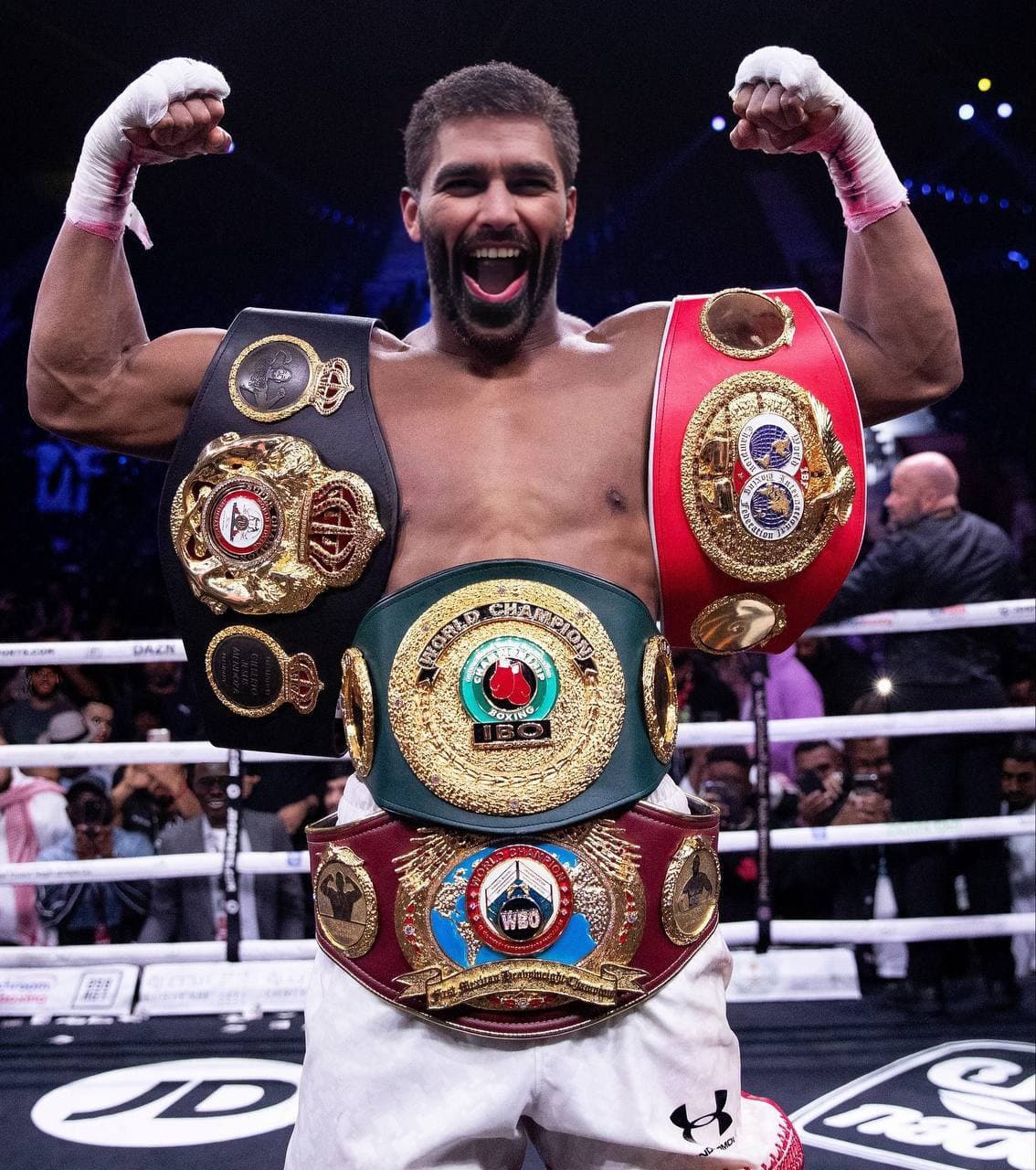 Boxer celebrating with multiple championship belts in the ring.