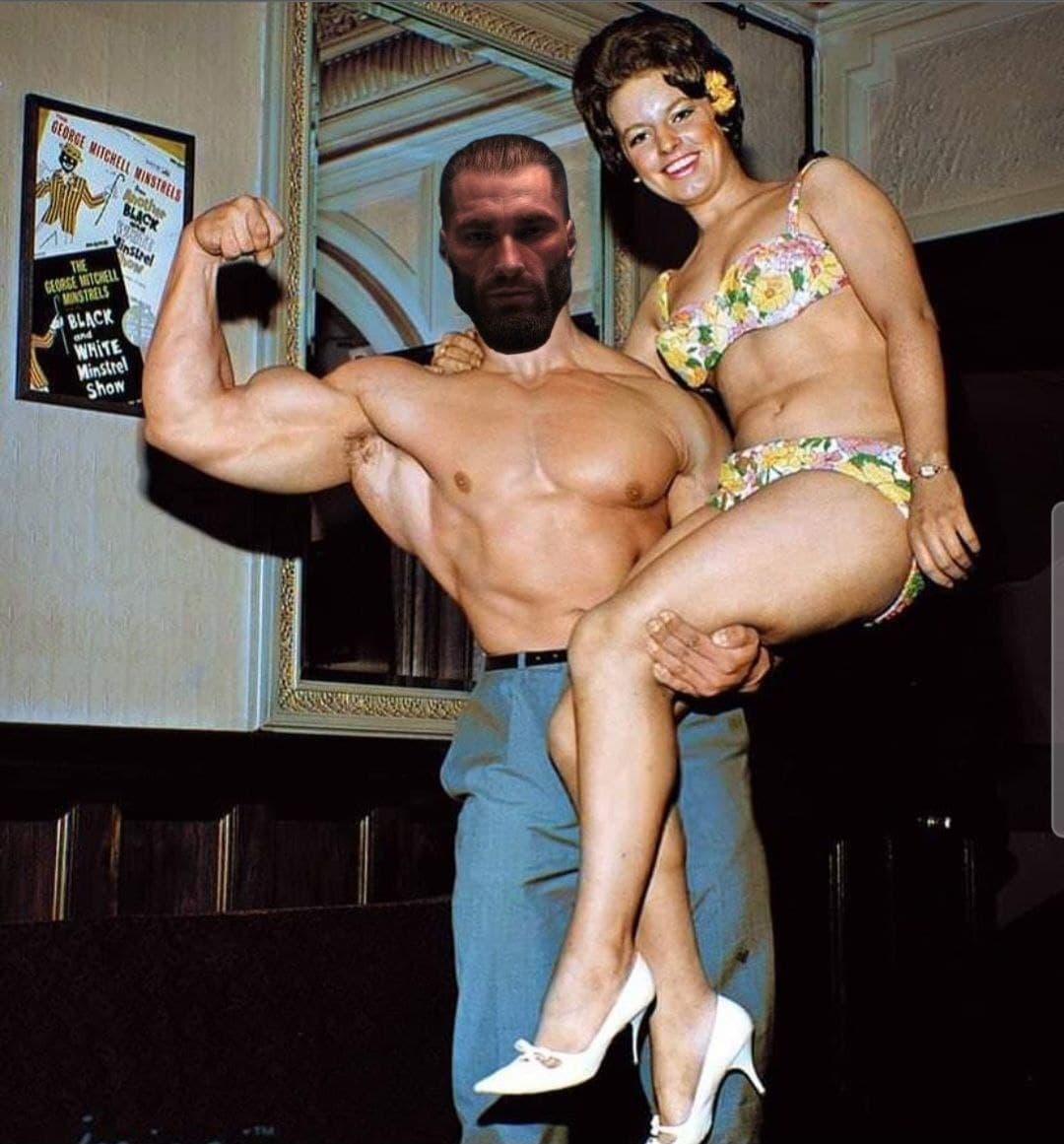Muscular man holds woman in bikini, flexing his bicep.