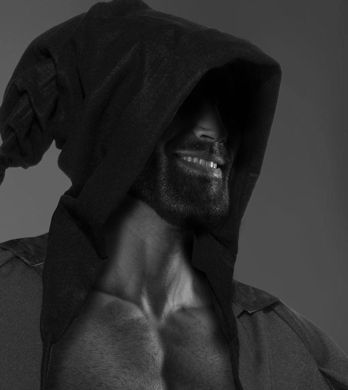 Muscular man in a dark hood smiling confidently.
