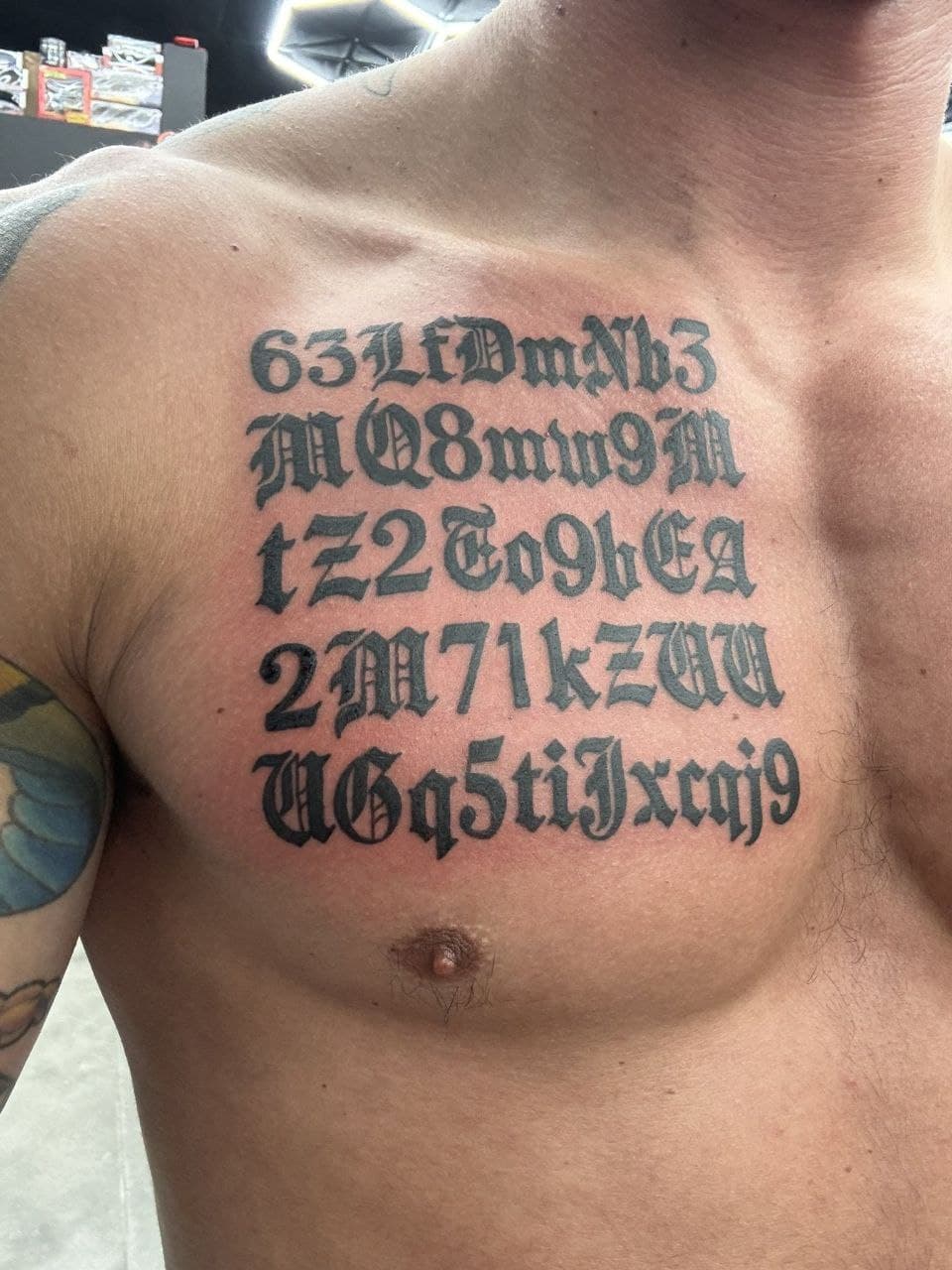 Muscular man with intricate chest tattoos of alphanumeric characters.