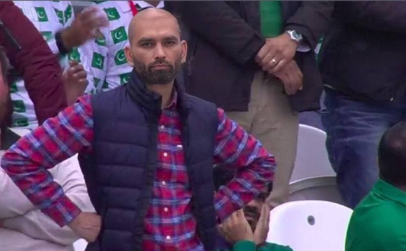 A man standing with crossed arms in a sports crowd.