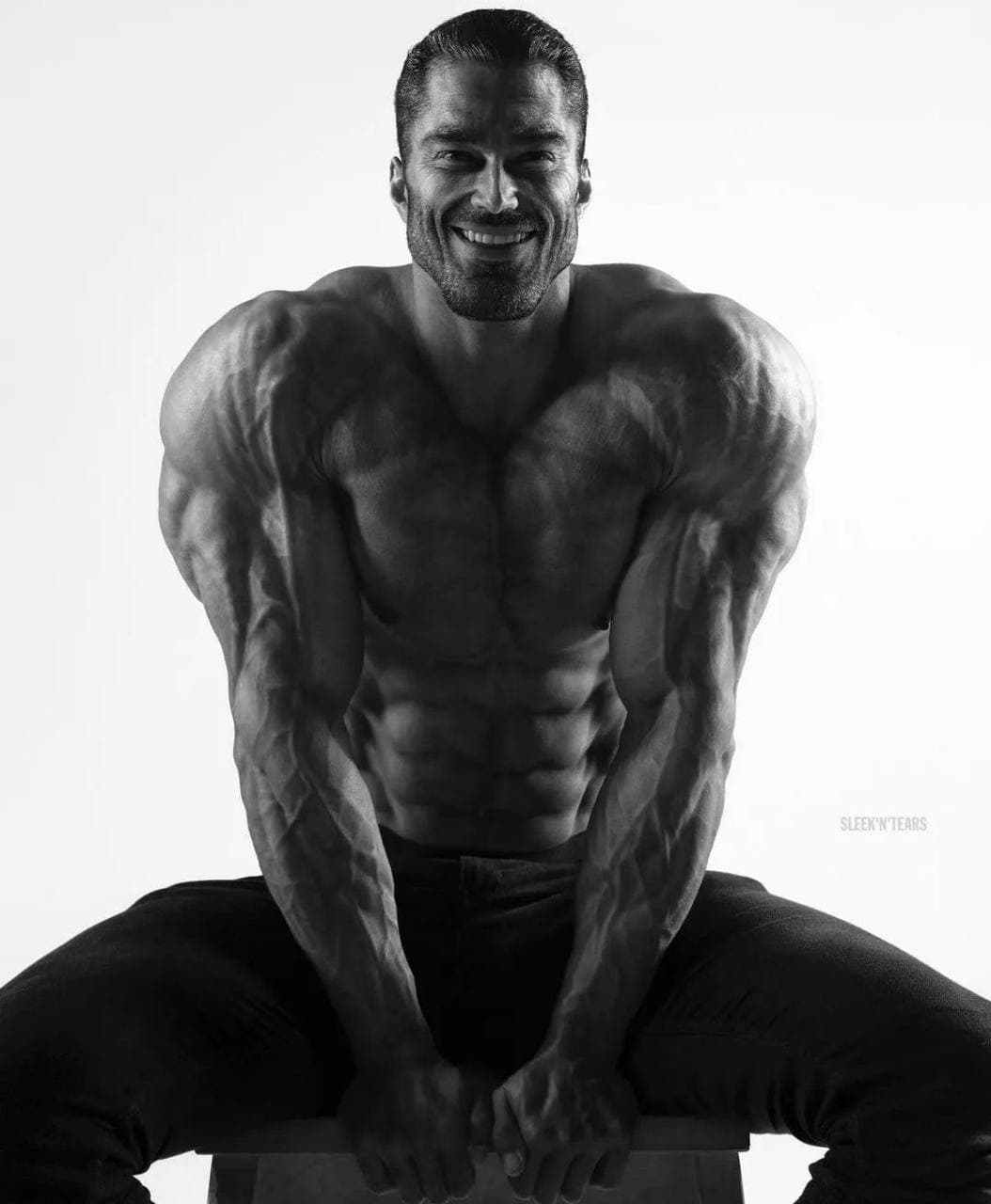 Muscular man smiling while sitting, showcasing his physique.
