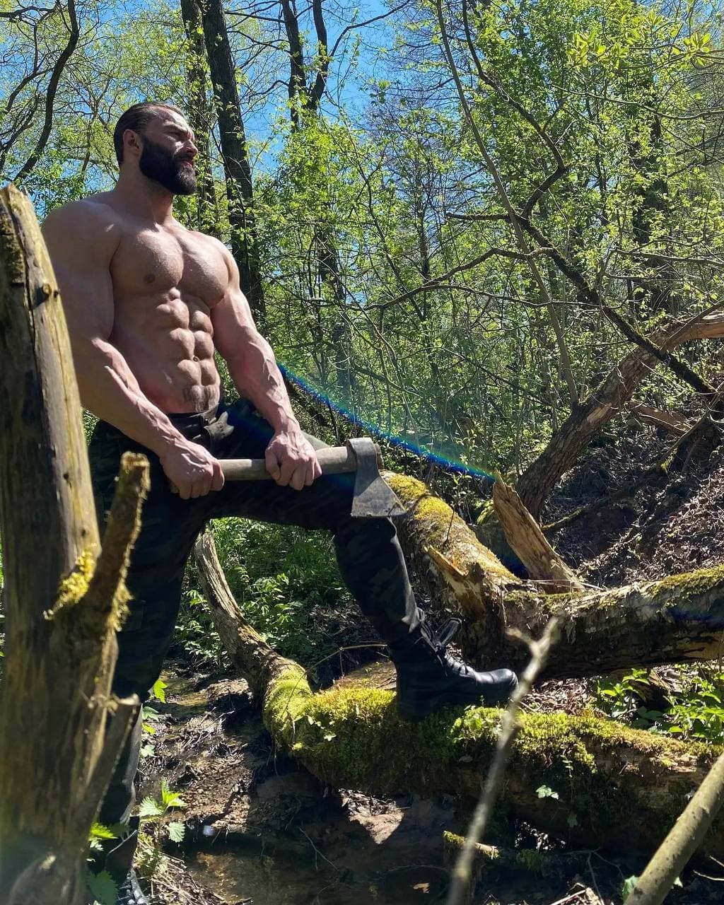 Muscular man holding an axe in a forest.