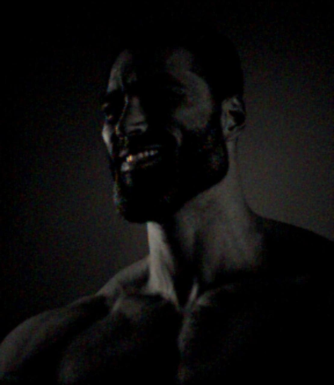 Muscular man smiling confidently in low light.