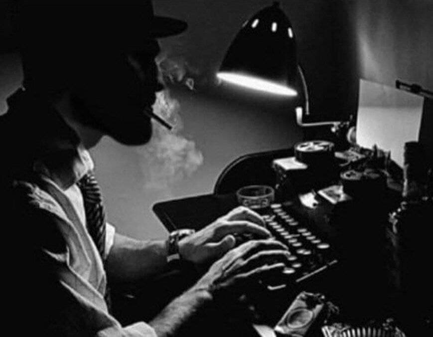 Man typing on a vintage typewriter in a dimly lit room.
