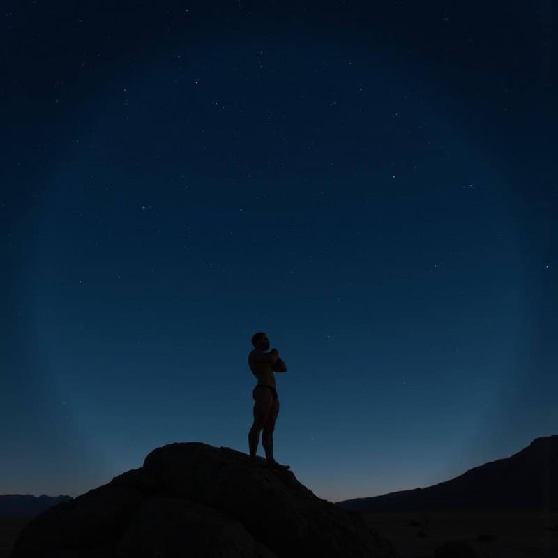 Silhouette of a muscular man on a rock under a starry sky.