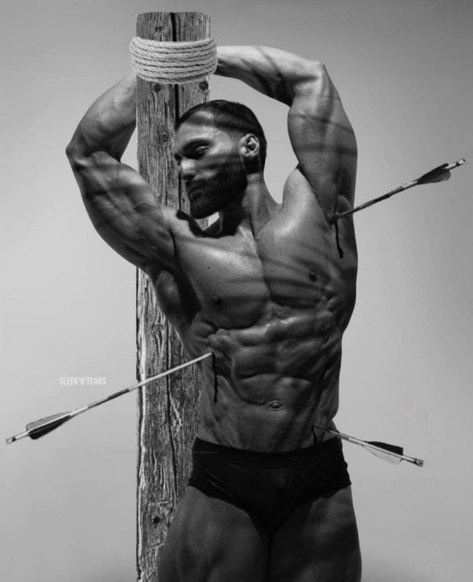 Muscular man posed with arrows on a wooden post.