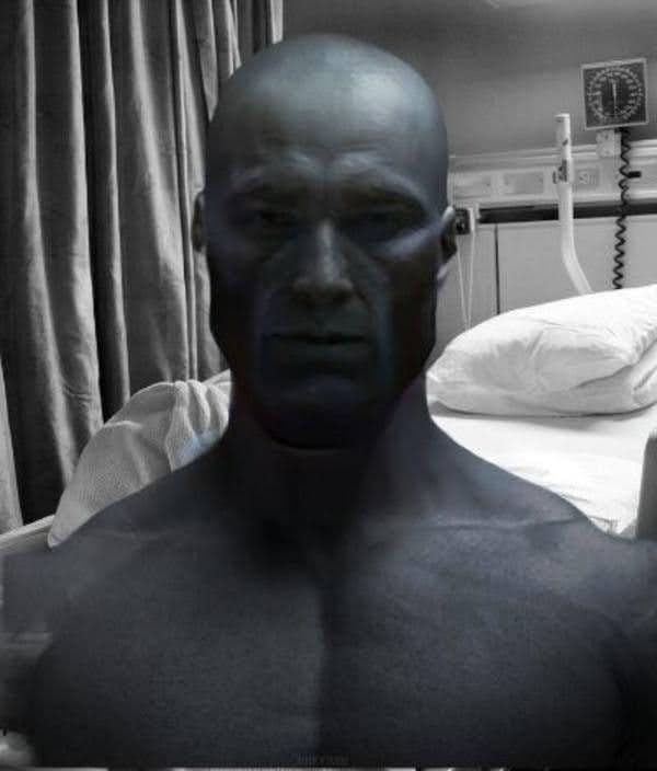 Muscular figure in a hospital room with a serious expression.