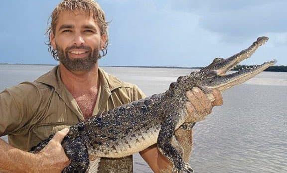 Man holding a crocodile with a confident expression.