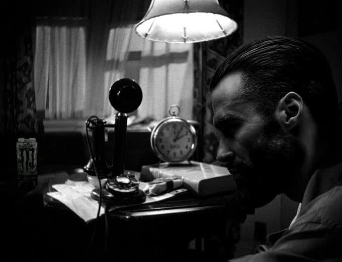 Intense man staring at a desk with a lamp and a phone.