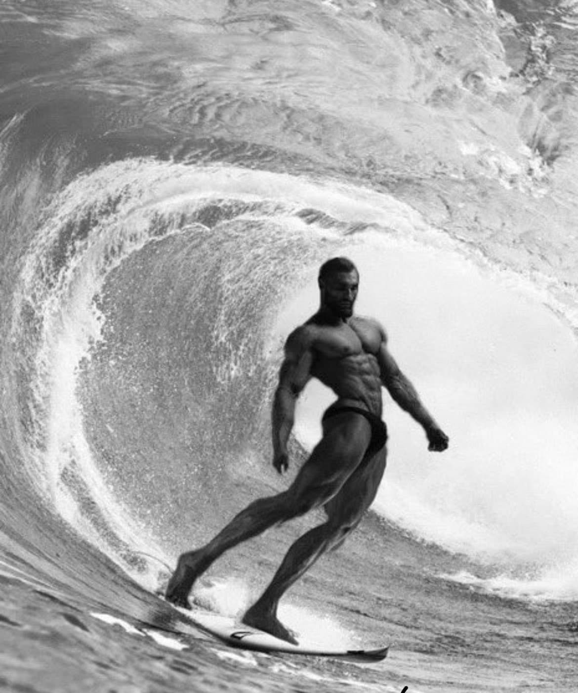 Muscular man surfing a large wave in black and white.