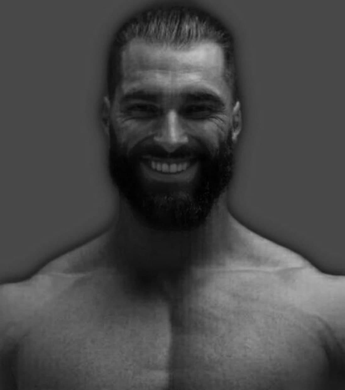 Muscular man with beard smiling against dark background.