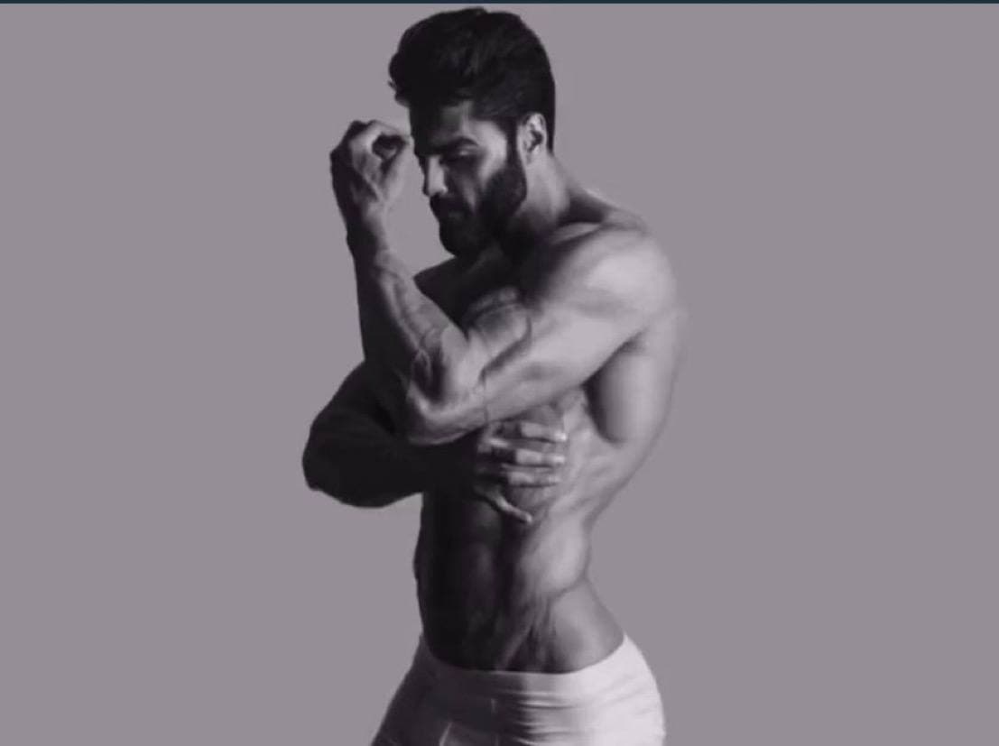 A muscular man poses confidently against a gray background.