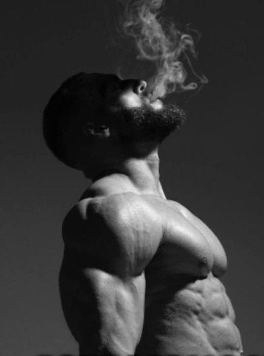 Muscular man exhaling smoke against a black and white backdrop.