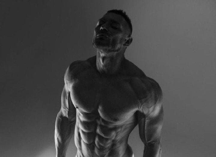 Powerful man showcasing impressive physique in dark lighting.