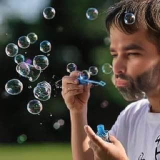Man with beard blowing bubbles outdoors.