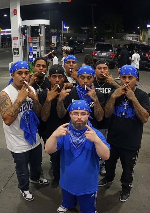 Group of men in blue bandanas striking poses at a gas station.