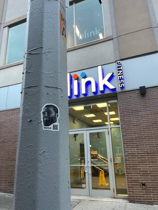 GigaChad sticker on a streetlight near a gym.