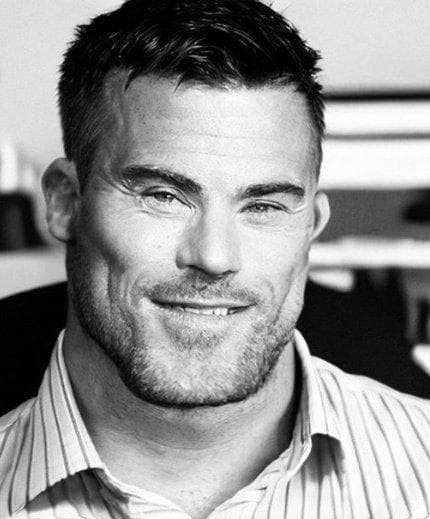 A muscular man smiling confidently in a striped shirt.