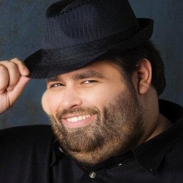 Man in a fedora smiling and tipping his hat.
